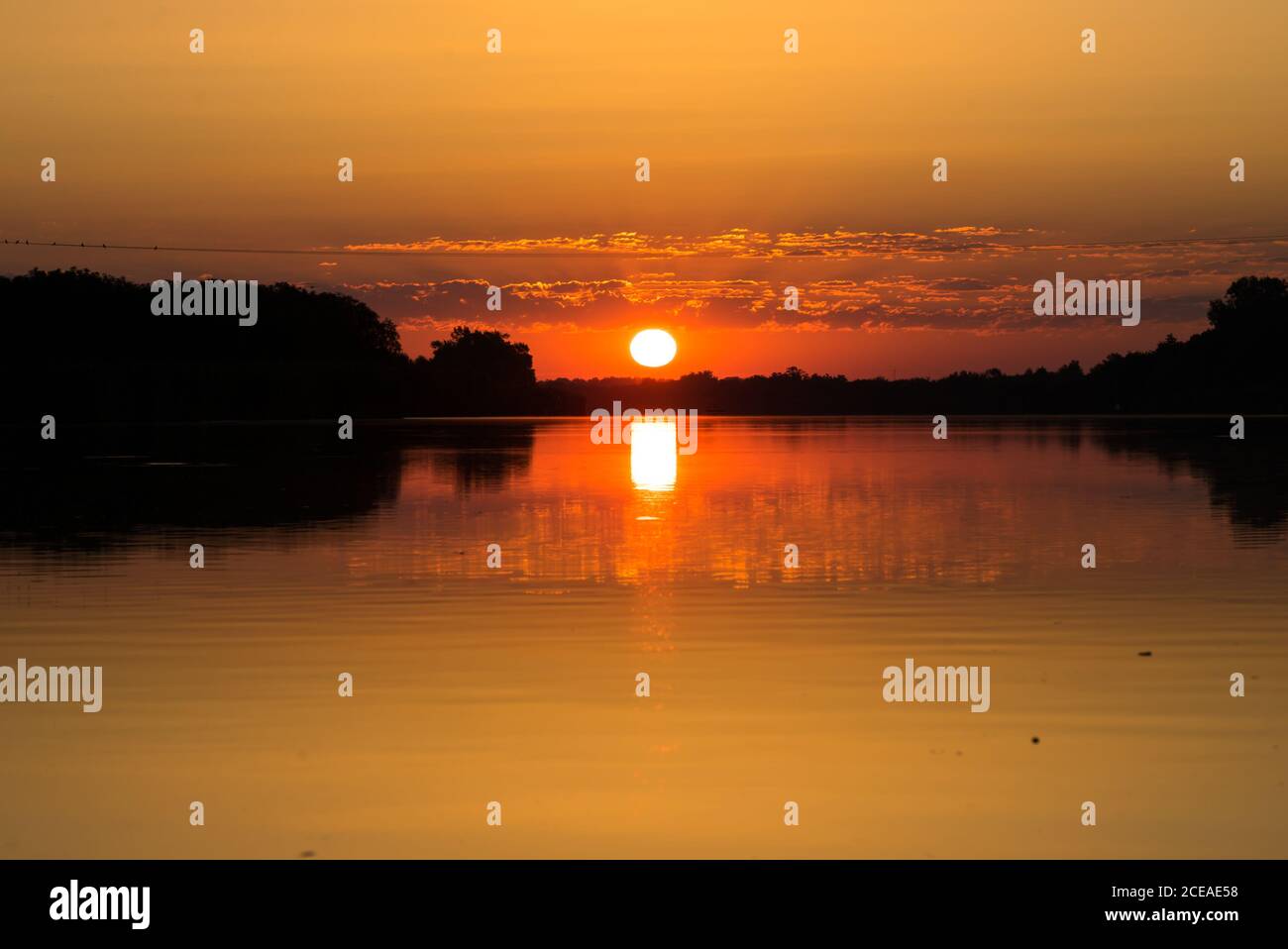 Schöner Sonnenaufgang über dem Fluss, See. Die orangefarbene Sonnenscheibe wird auf der Wasseroberfläche reflektiert. Stockfoto