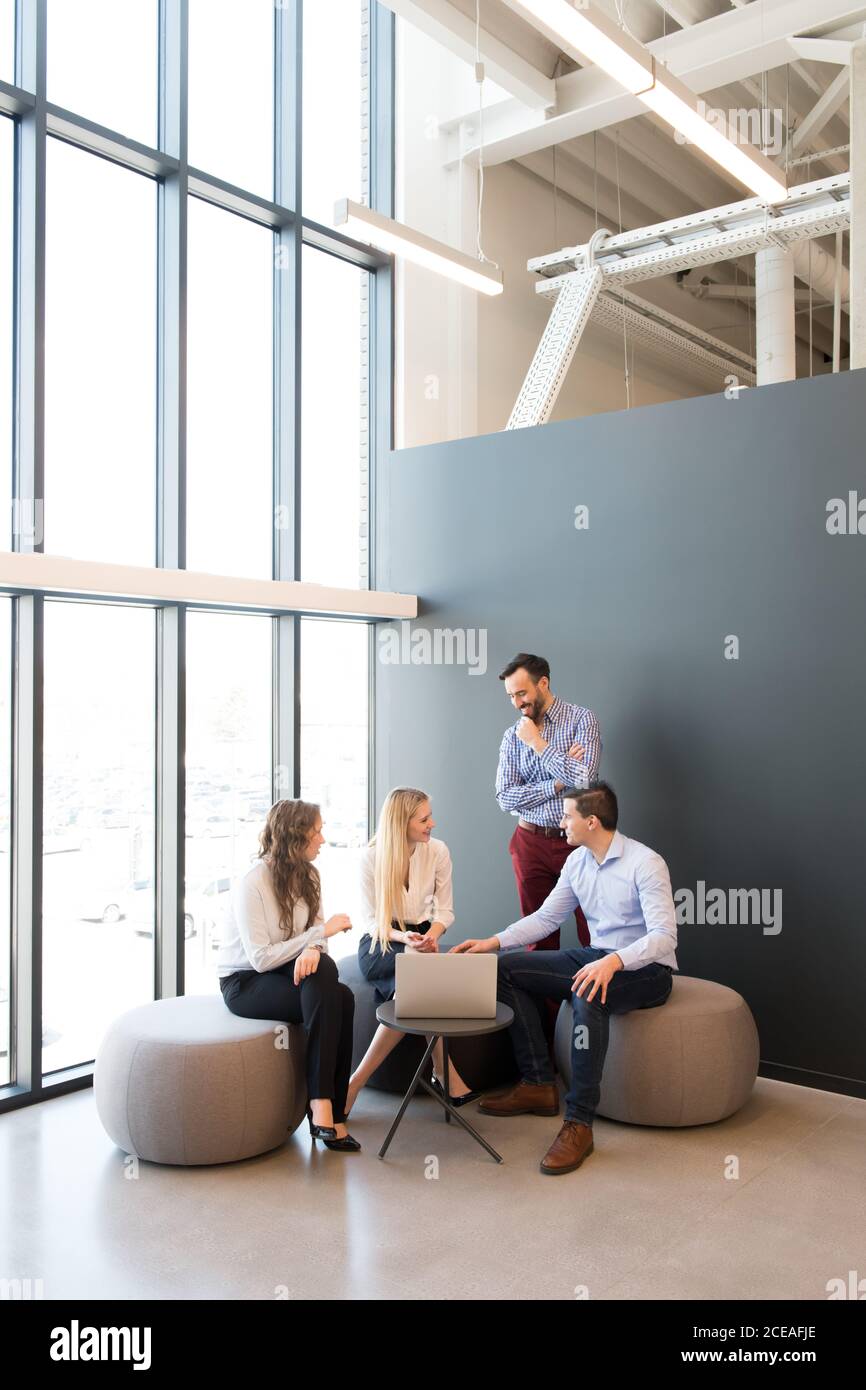 Stilvolle Frauen und Männer sitzen zusammen um Laptop auf klein Tisch und Gespräch während des Meetings Stockfoto
