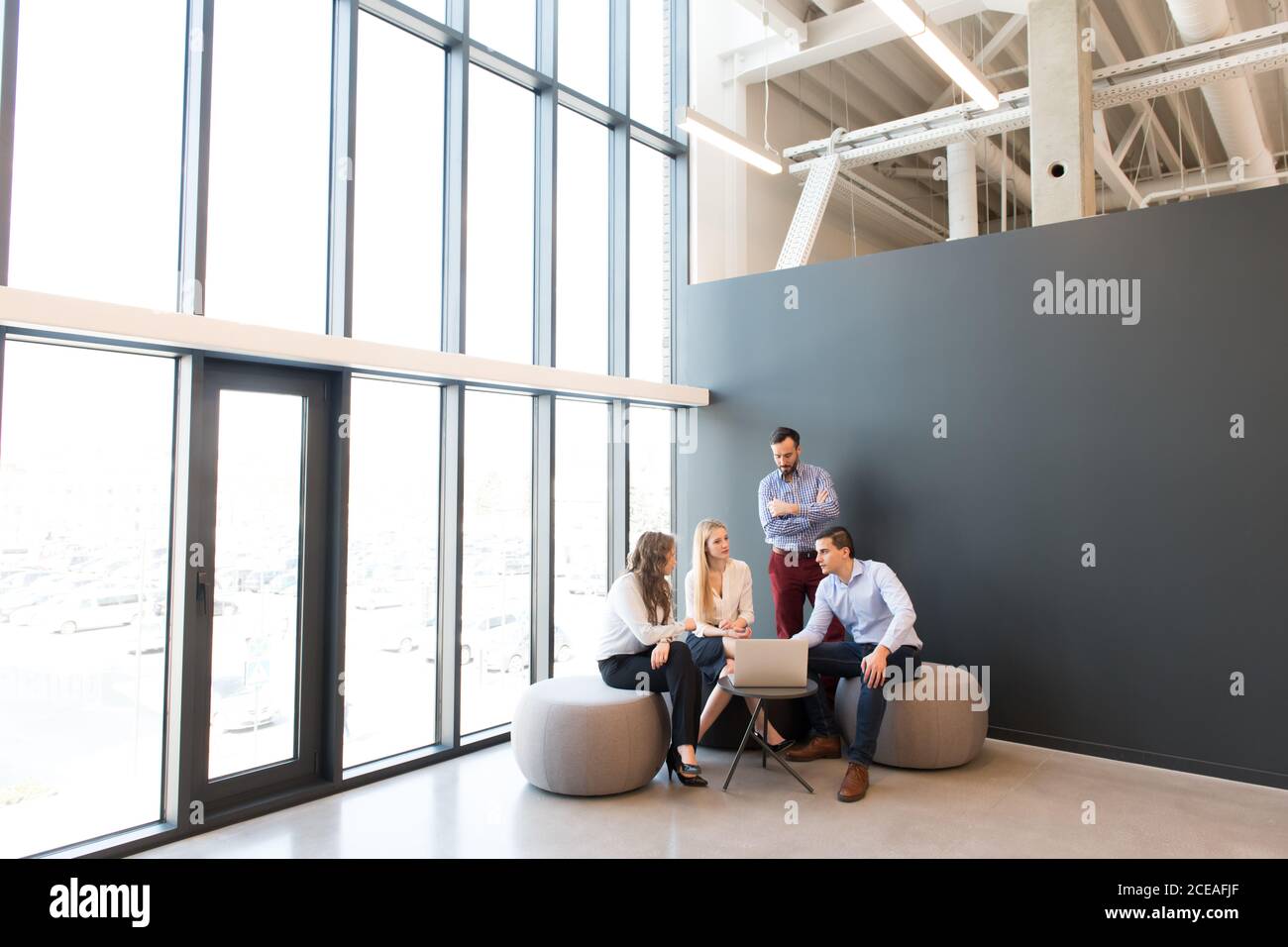 Stilvolle Frauen und Männer sitzen zusammen um Laptop auf klein Tisch und Gespräch während des Meetings Stockfoto