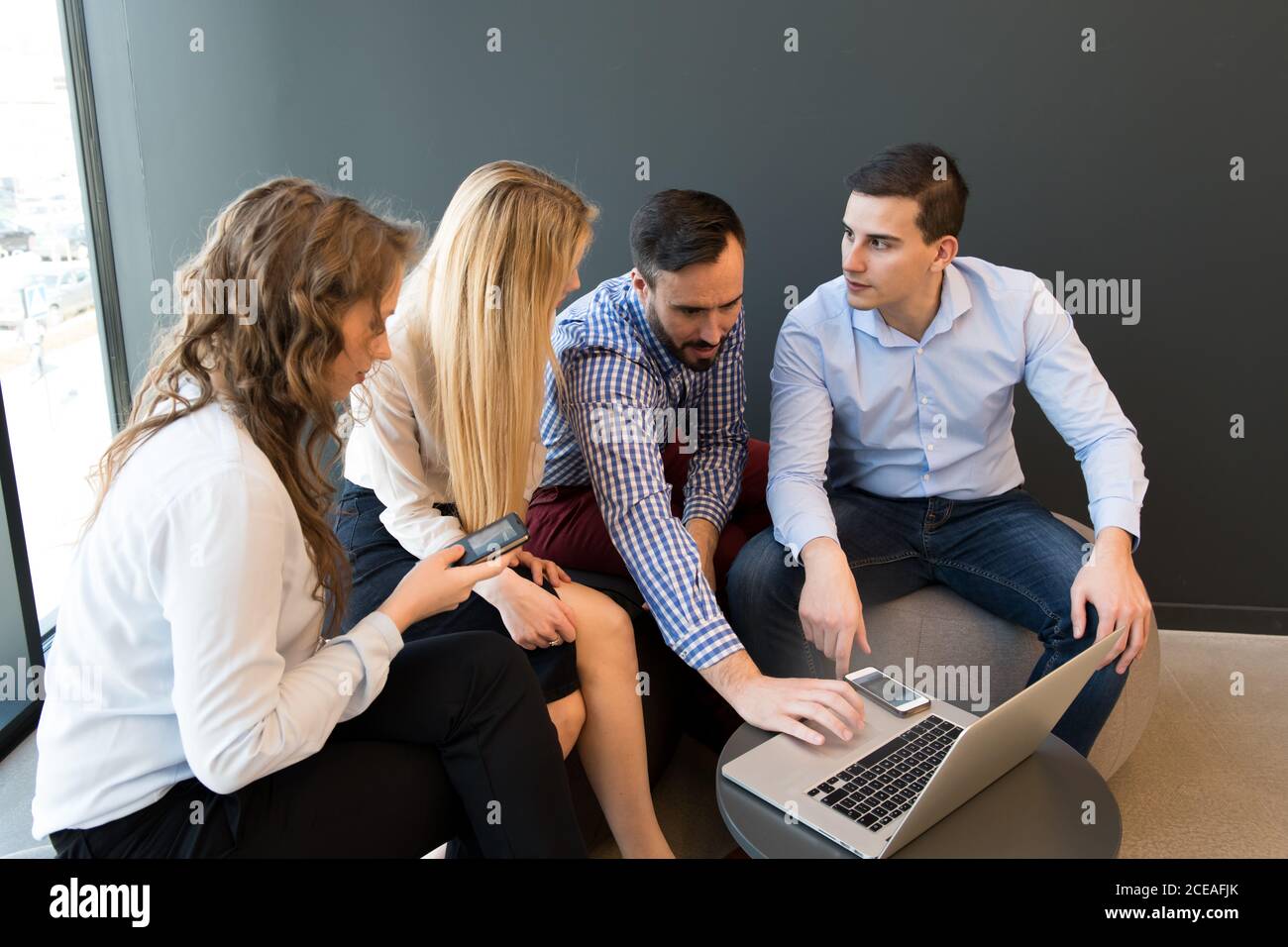 Stilvolle Frauen und Männer sitzen zusammen um Laptop auf klein Tisch und Gespräch während des Meetings Stockfoto