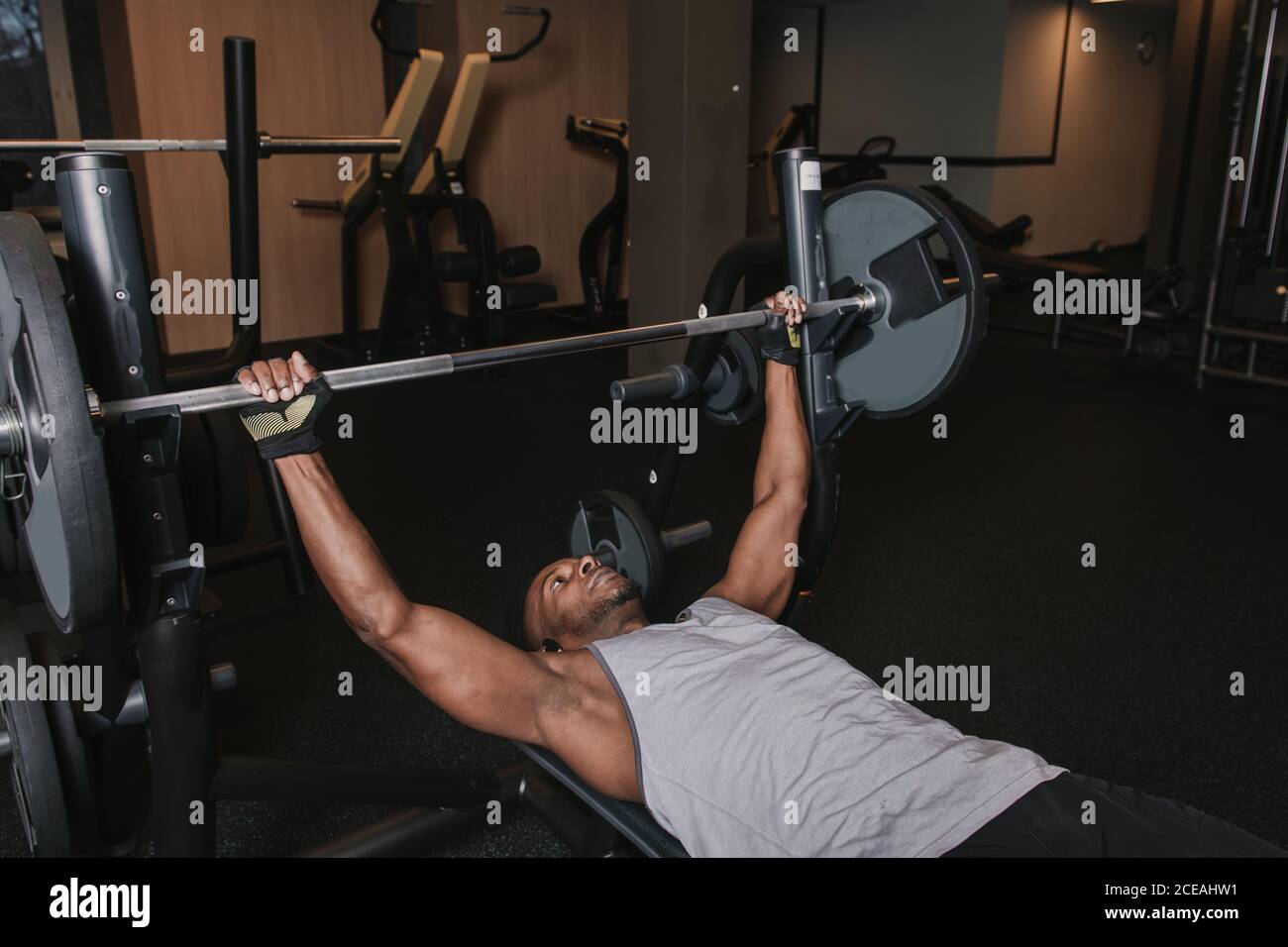 Schöner afrikanischer?amerikanischer Mann in Sportkleidung, der auf Bank liegt und hebt Schwere Langhantel beim Training im modernen Fitnessstudio Stockfoto