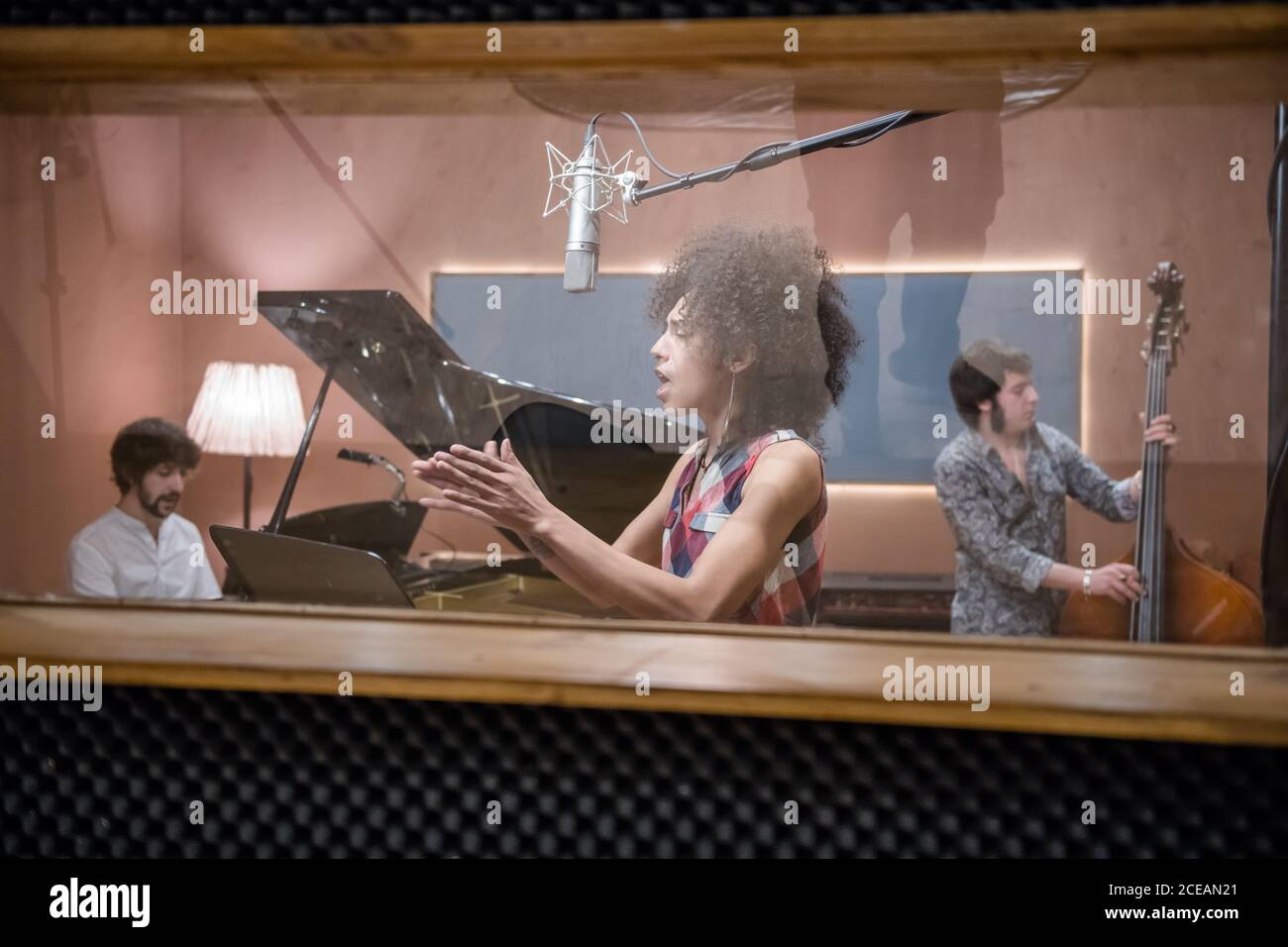 Attraktive Frau singt Lied und klatscht Hände, während sie mit der Band im Aufnahmestudio probt. Stockfoto