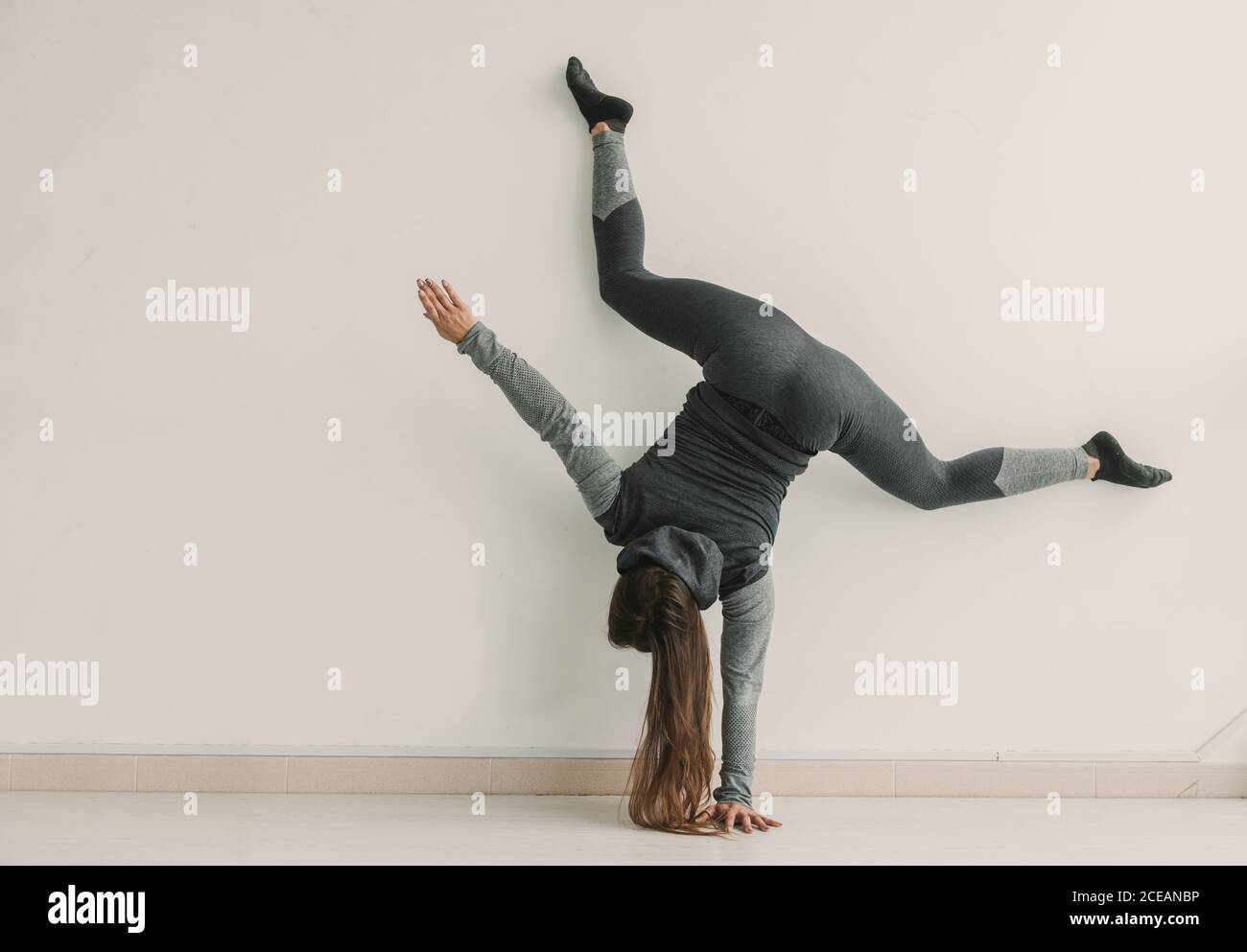 Rückansicht einer jungen sportlichen Frau, die im hellen Raum Handstand und Bein gespalten macht Stockfoto