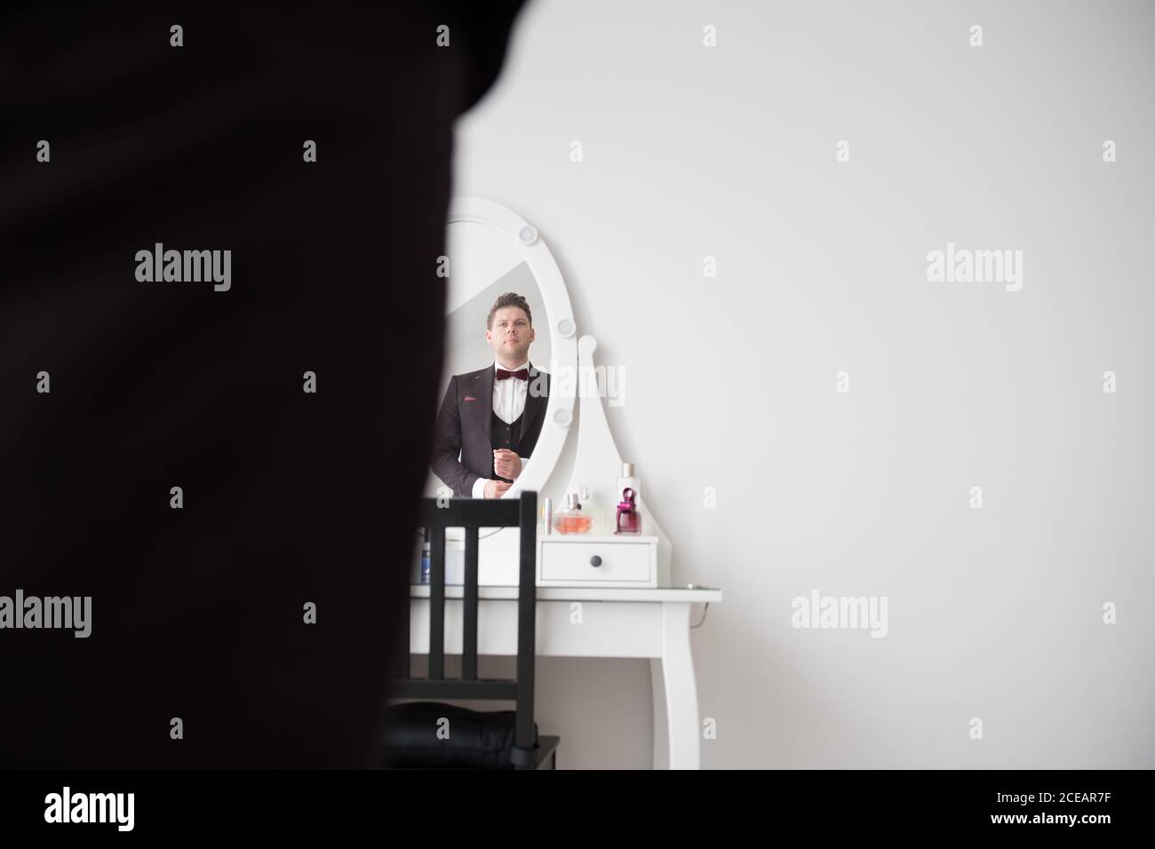 Spiegelung von jungen schönen Mann in schwarz formalen Kostüm stehen Im Zimmer vor dem Frisiertisch mit Spiegel Stockfoto