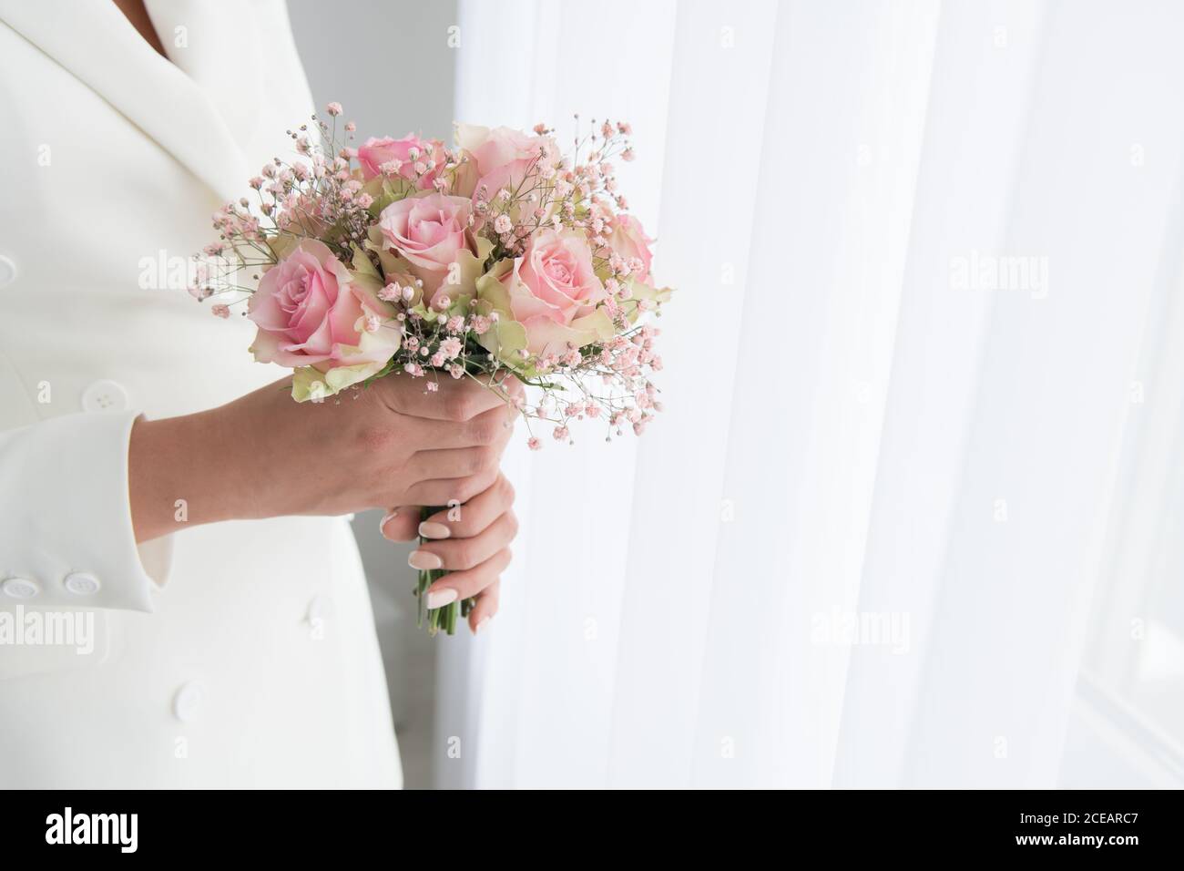 Gesichtslose Aufnahme einer Frau in einem eleganten Brautanzug mit kleinem Strauß mit Rosen Stockfoto