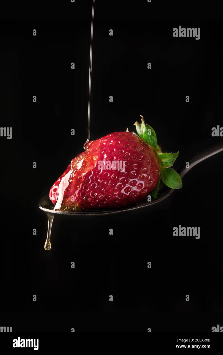 Nahaufnahme von frischen reifen roten Erdbeeren in fließendem Honigsirup auf schwarzem Hintergrund. Stockfoto