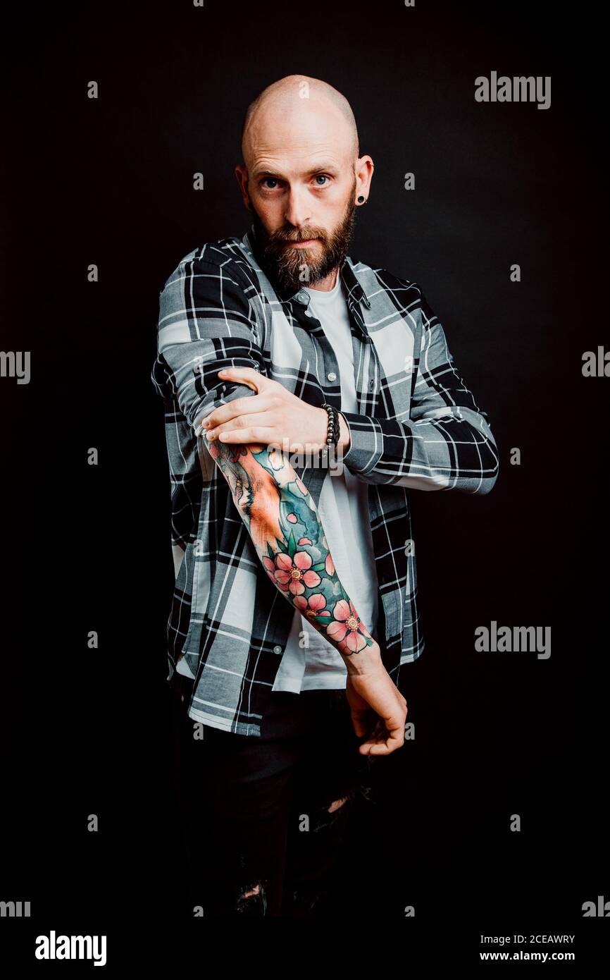 Bärtige haarlose Hipster in Shirt mit Tattoos auf Arme auf schwarzem Hintergrund Stockfoto