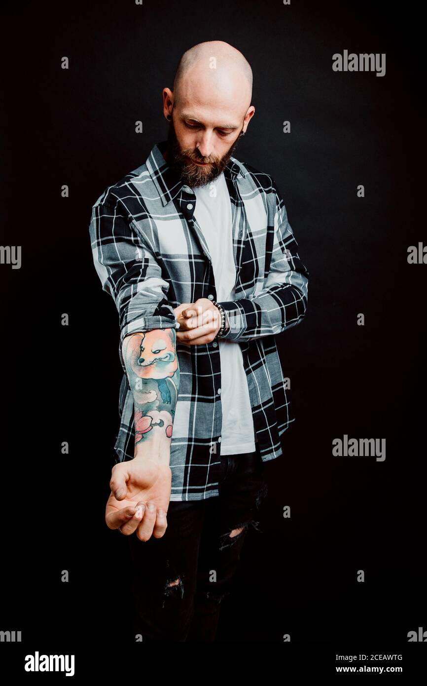 Bärtige haarlose Hipster in Shirt mit Tattoos auf Arme auf schwarzem Hintergrund Stockfoto