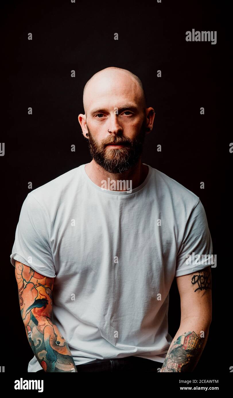 Unbehaarte Hipster in t Bärtigen-shirt mit Tattoos auf Arme auf schwarzem Hintergrund Stockfoto