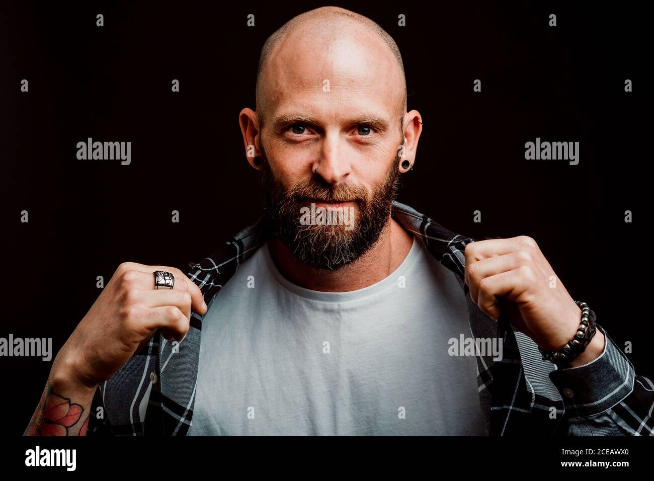Bärtige haarlose Hipster in Shirt mit Tattoos auf Arme auf schwarzem Hintergrund Stockfoto