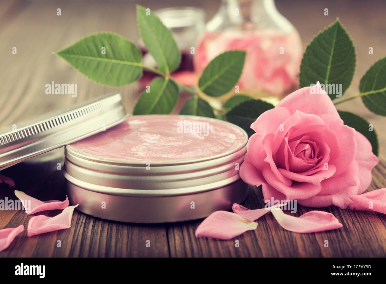 Glas mit einer hausgemachten feuchtigkeitsspendenden Beauty-Creme und rosa Rosenblüte. Herstellung von kosmetischen Produkten zu Hause. Stockfoto