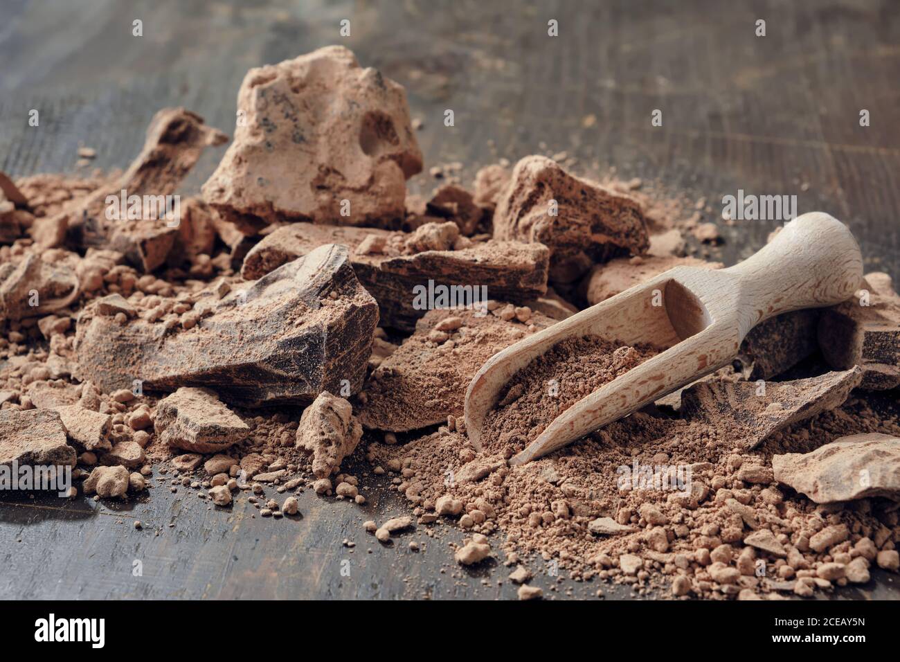 Stücke geriebener Kakao. Naturschokoladenklumpen und Holzlöffel auf dunklem Holztisch. Stockfoto