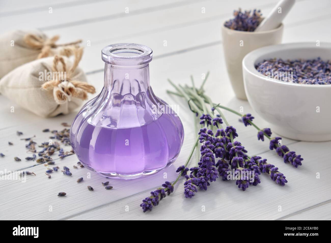 Trockene Lavendelblüten, Flasche ätherisches Öl oder aromatisiertes Wasser, Beutel und Mörtel auf weißem Holztisch. Stockfoto