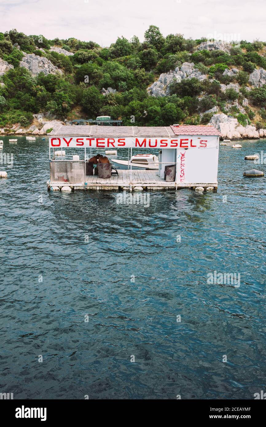 Blauer plätschernder See mit kleinem schwimmenden Restaurant im Hintergrund Felsen mit grünen Büschen bedeckt Stockfoto