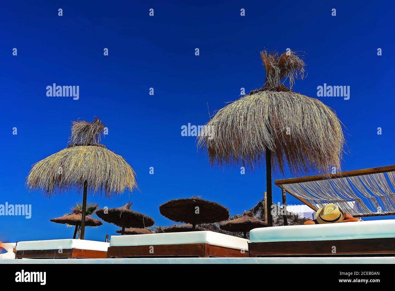 Schöne Heuschirme stehen am Luxusstrand auf dem Hintergrund des klaren blauen Himmels. Stockfoto