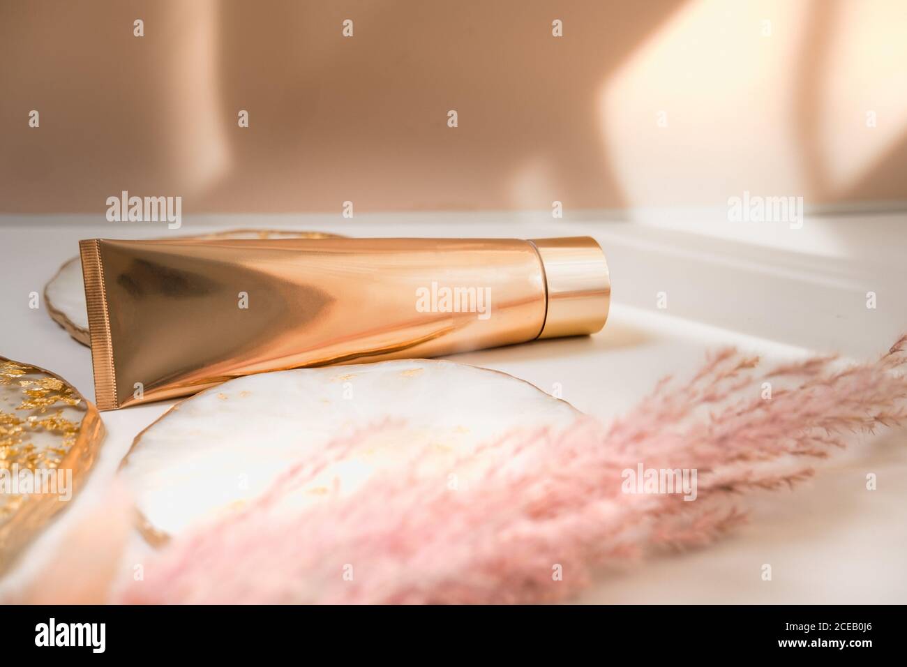 Goldene Kosmetikröhre Licht Pastellfarbe Hintergrund, Lichter und Schatten. Minimalistisches Styling, Stillleben. Beauty Blogging, Branding Layout, Hautpflege ad m Stockfoto