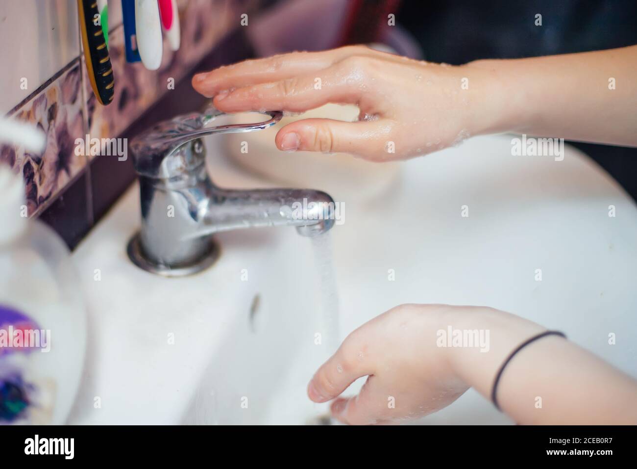 Kind schließt Wasserhahn mit fließendem Wasser. Wasser sparen. Reinigungshand, um die Ausbreitung von Covid-19, Coronavirus Pandemie zu stoppen Stockfoto