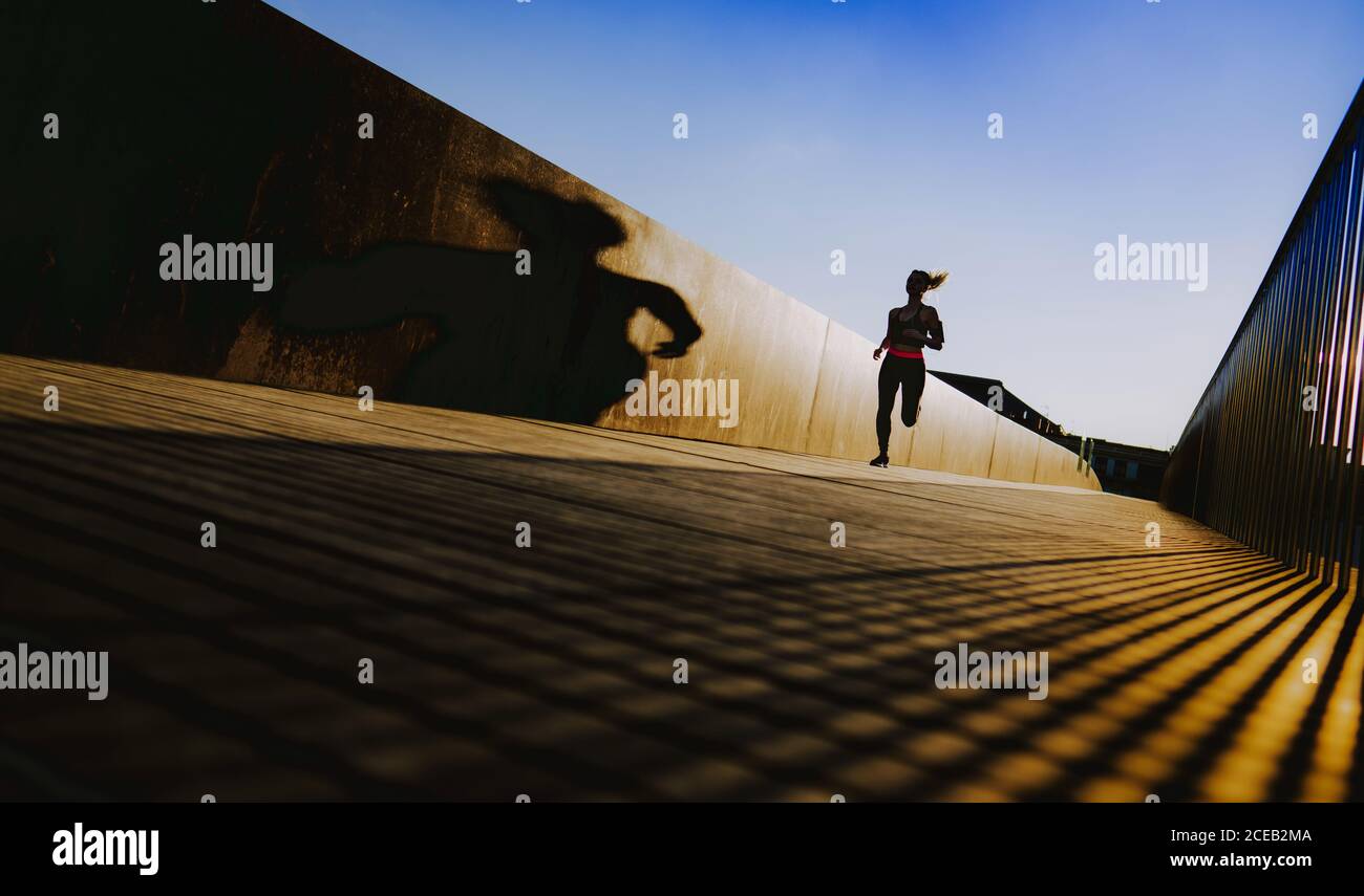 Junge Dame in Sportkleidung auf Wanderweg in sonniges Wetter mit blauem Himmel läuft Stockfoto
