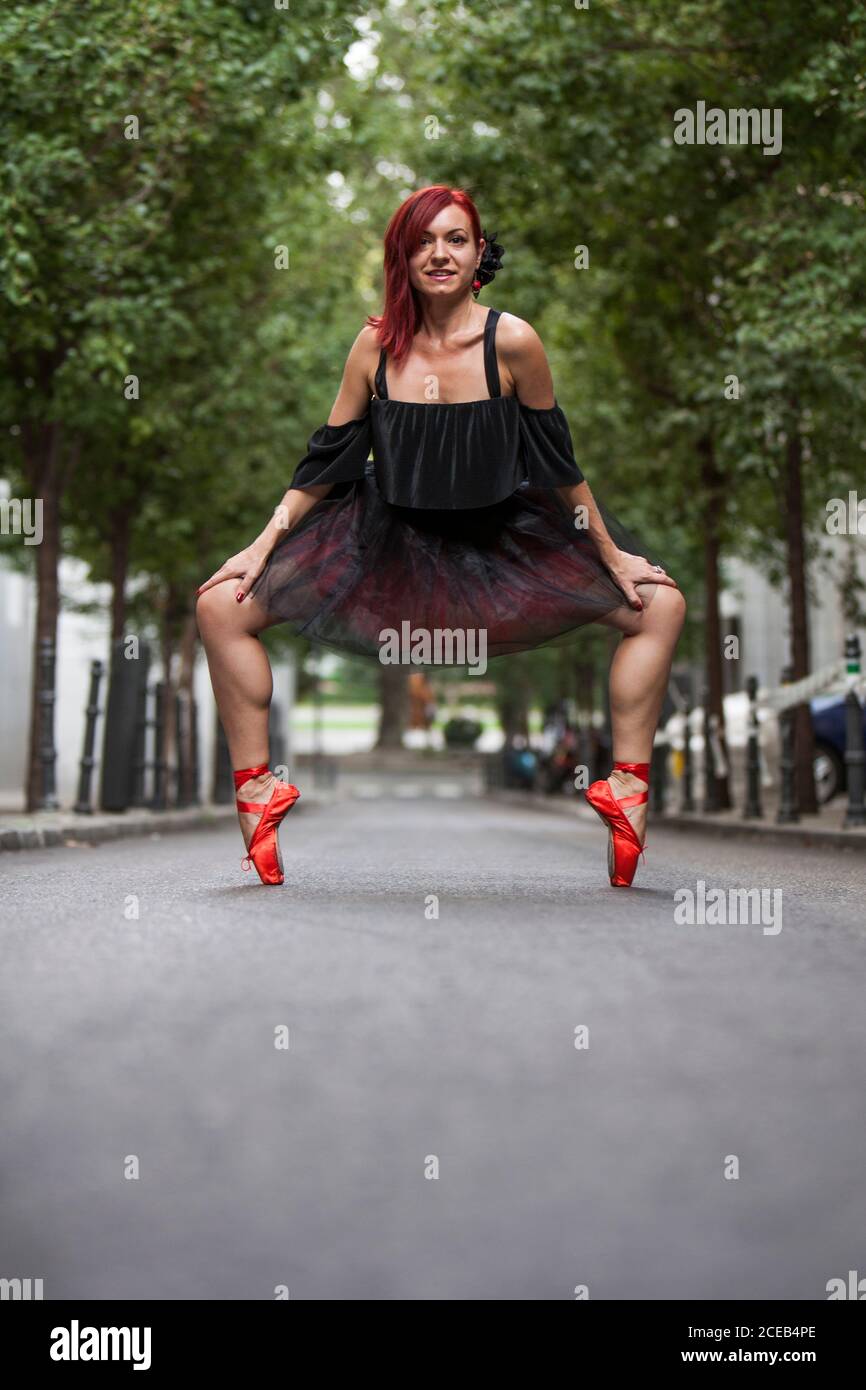 Roter Kopf Ballerina mit schwarzem Tutu und roten Ballett Tipps tanzen auf der Straße mit Bäumen im Hintergrund. Stockfoto