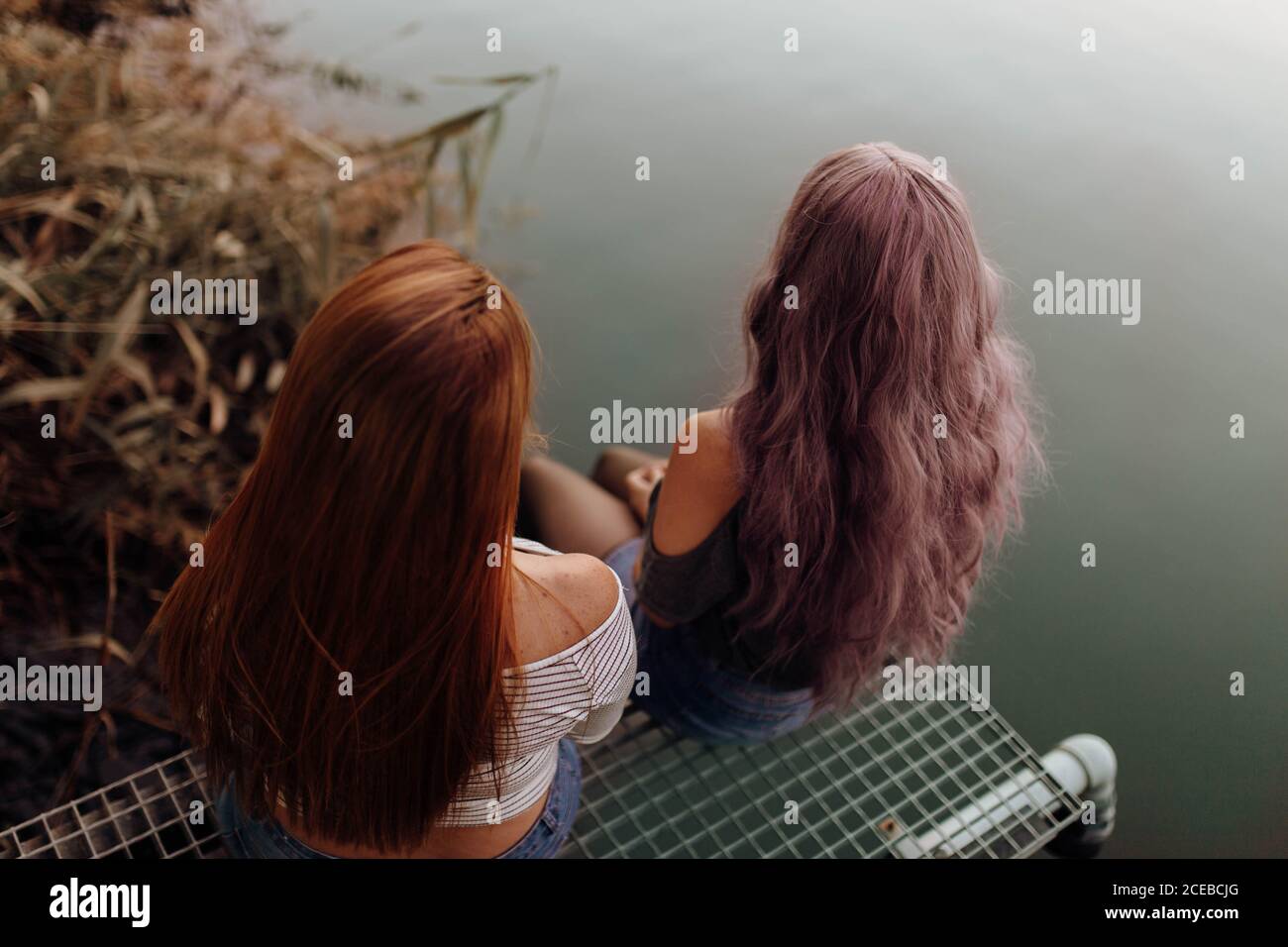 Form oben Rückansicht von jungen Frauen mit langen Haaren Sitzen zusammen über dem Wasser des ruhigen Sees Stockfoto