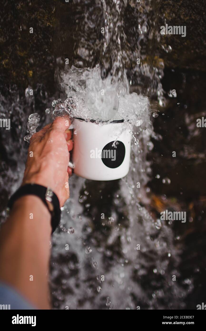 Nahaufnahme der Hand eines anonymen Mannes, der den Becher unter sich hält Frisches Wasser aus kaltem Wasser Quelle in der Natur Stockfoto