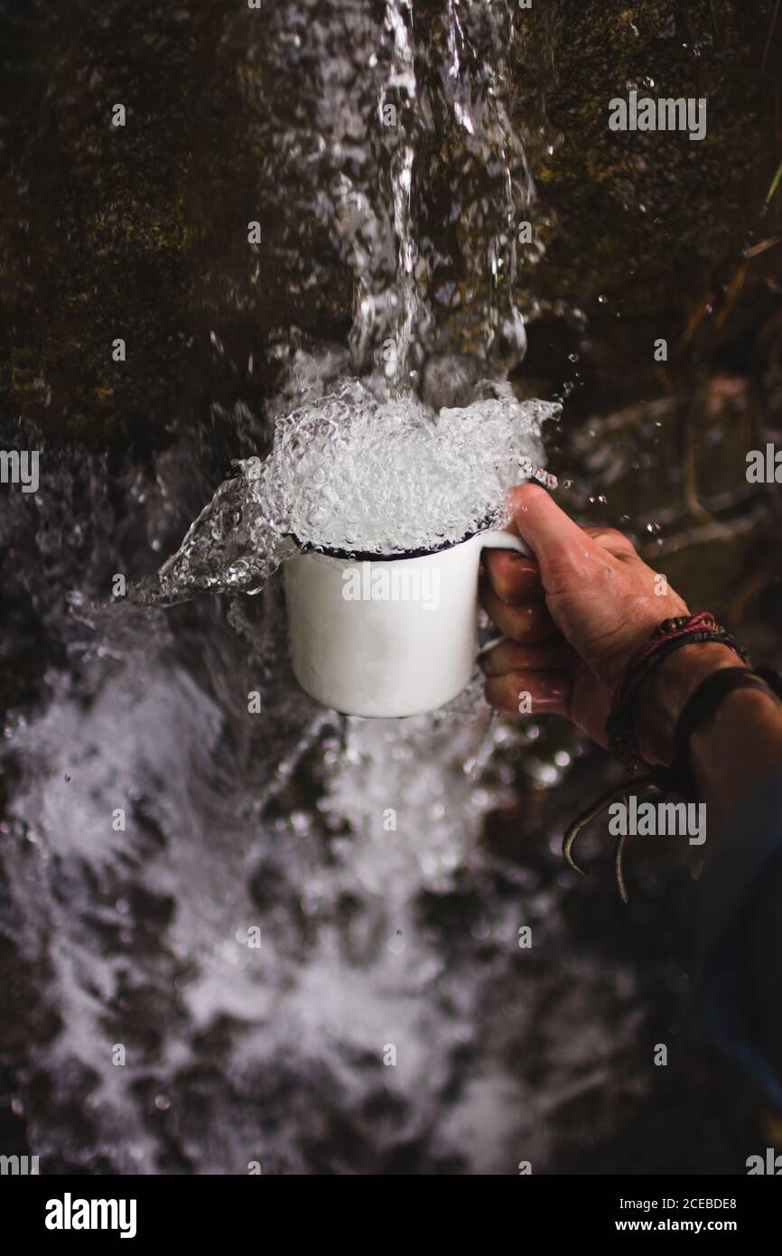 Nahaufnahme der Hand eines anonymen Mannes, der den Becher unter sich hält Frisches Wasser aus kaltem Wasser Quelle in der Natur Stockfoto