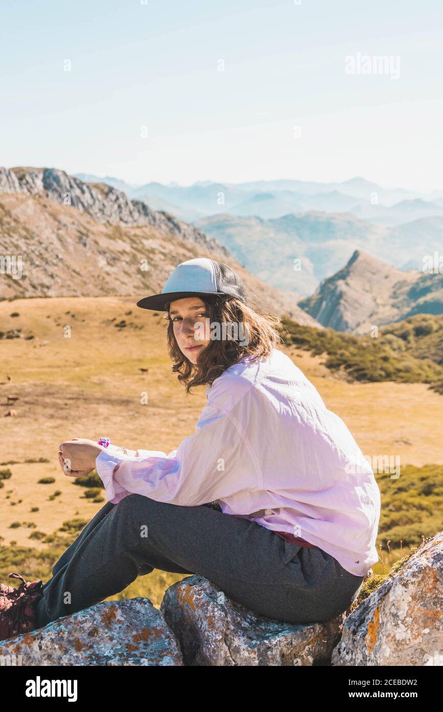 Seitenansicht einer Frau, die auf hohen Felsen über dem malerischen Tal mit Bergen im Herbstsonnenlicht sitzt Stockfoto