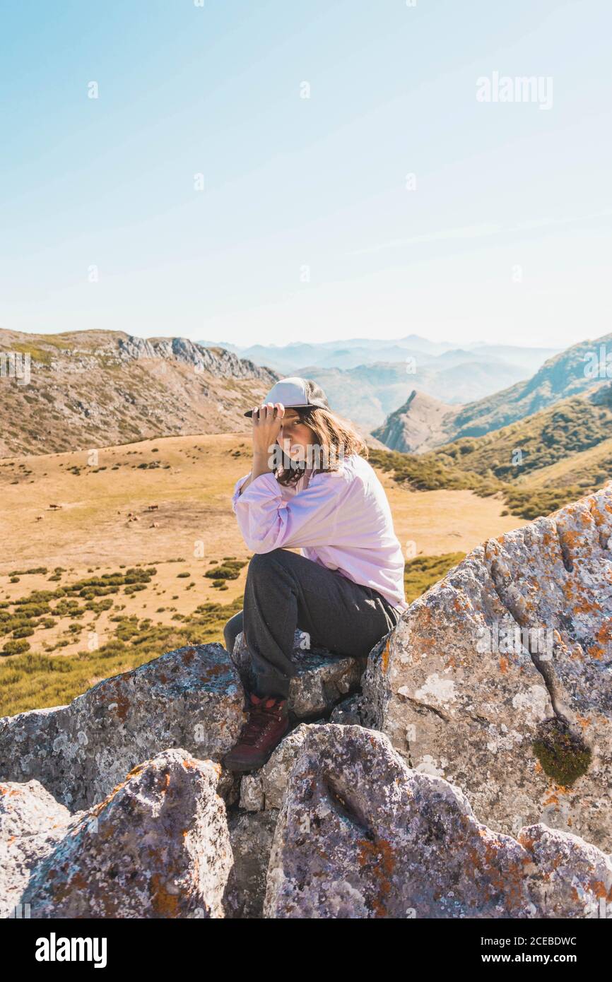Seitenansicht einer Frau, die auf hohen Felsen über dem malerischen Tal mit Bergen im Herbstsonnenlicht sitzt Stockfoto