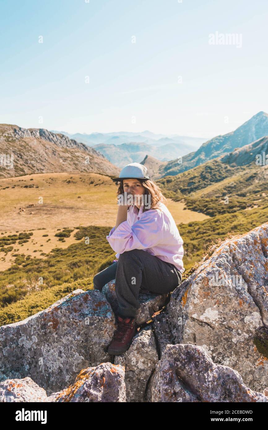 Seitenansicht einer Frau, die auf hohen Felsen über dem malerischen Tal mit Bergen im Herbstsonnenlicht sitzt Stockfoto