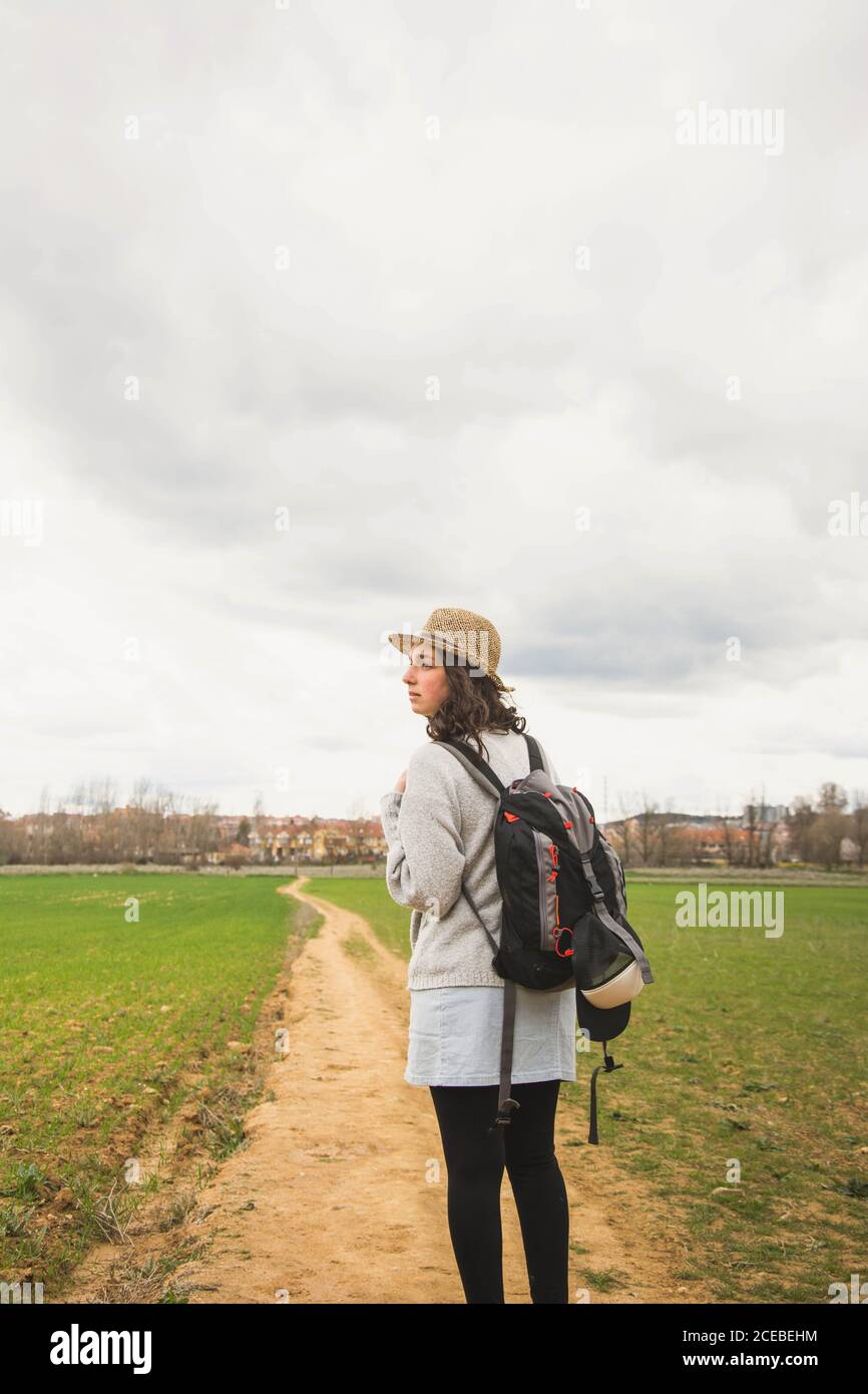 Attraktive junge Reisende Frau in Strohhut im grünen Feld stehen und wegschauen Stockfoto