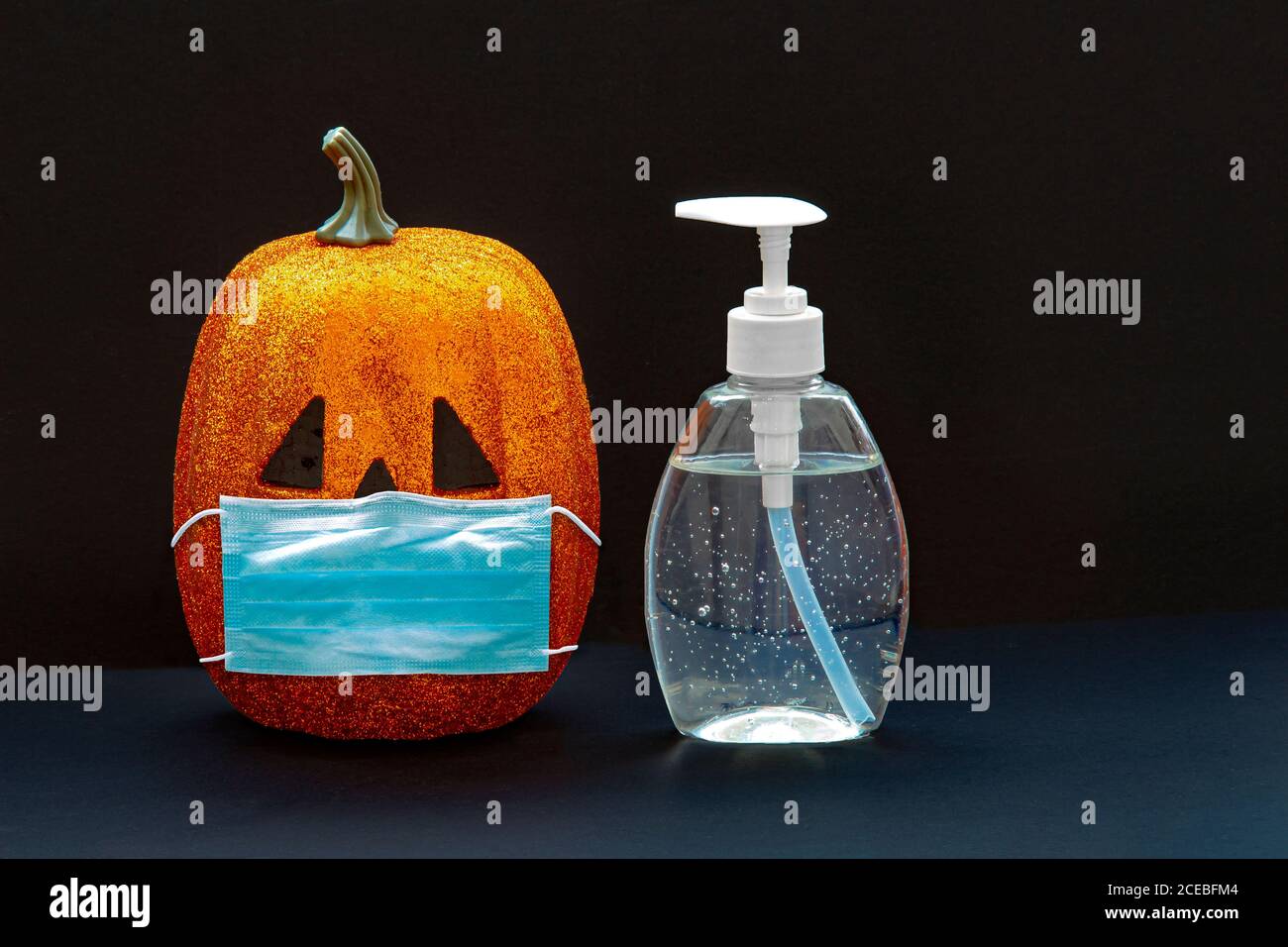 Jack-o-Laterne Kürbis Halloween trägt eine Gesichtsmaske mit Hand Desinfektionsflasche auf schwarzem Hintergrund. Konzept: Halloween während der globalen Pandemie. Covi Stockfoto