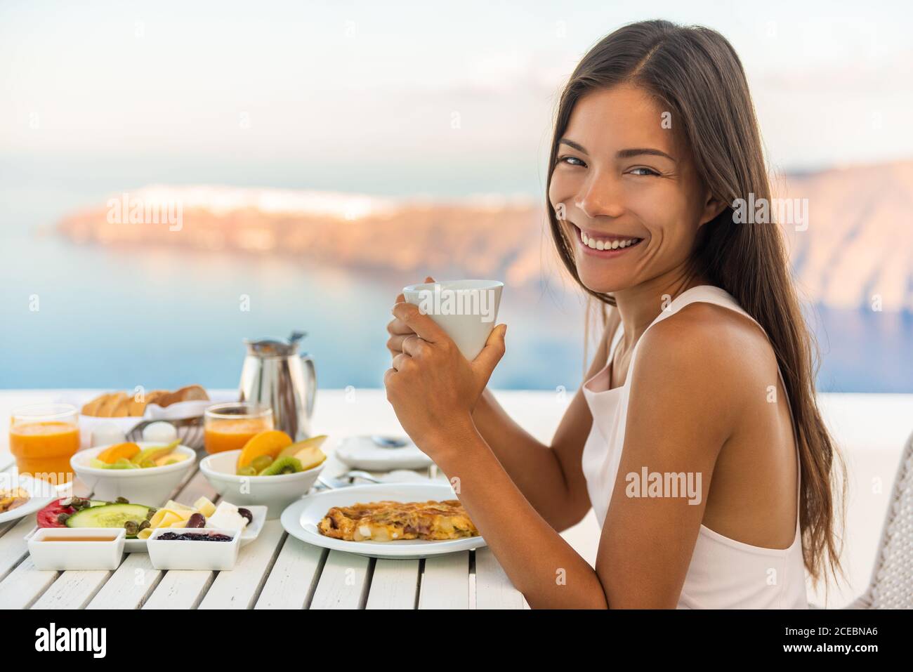Frühstück Frau beim Brunch im Luxushotelrestaurant mit Kaffeetasse und Blick auf das Mittelmeer vom Außenbalkon. Griechisches gesundes Essen Stockfoto