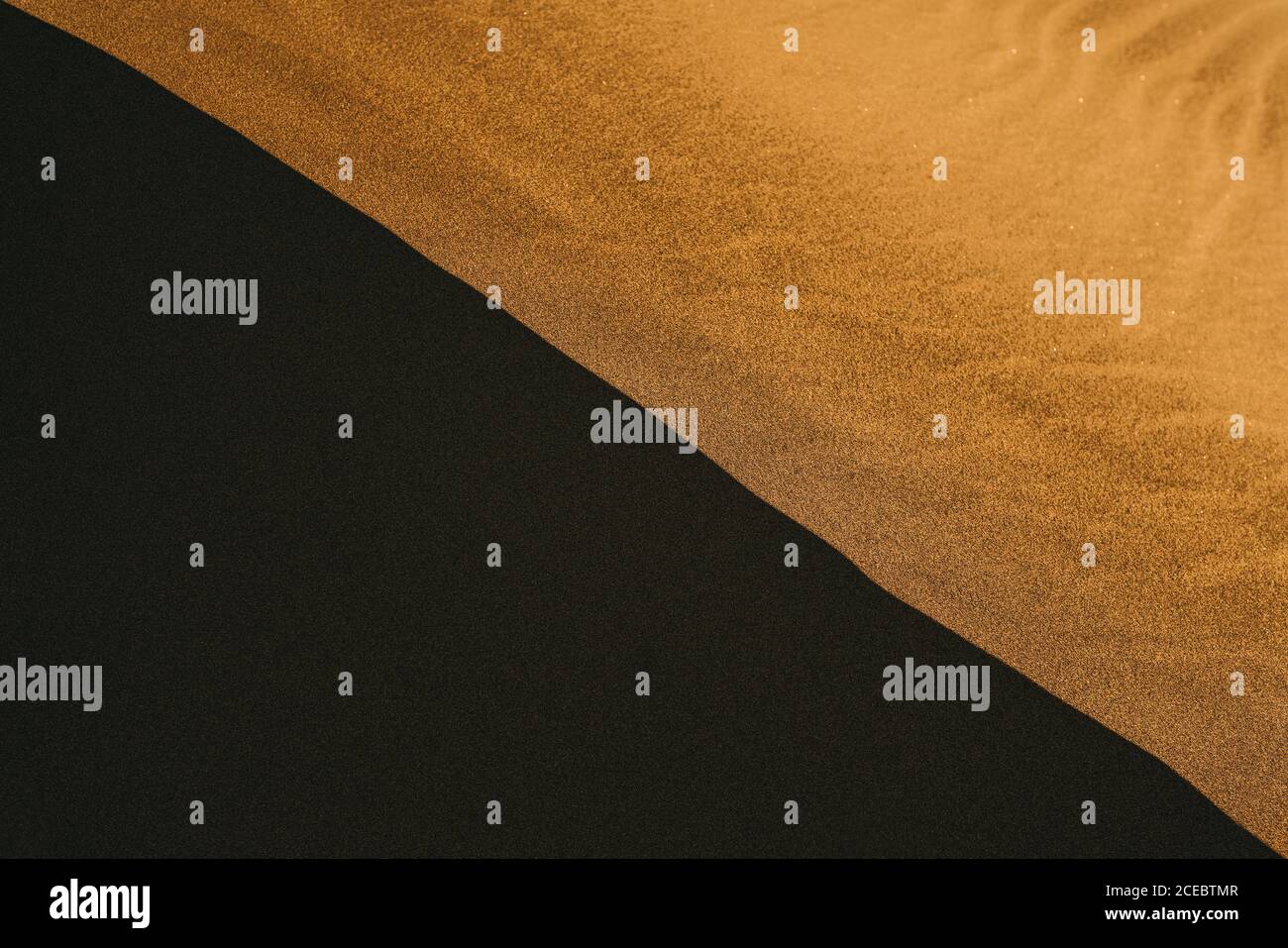 Wunderschöne, leuchtend orange Wüstensanddüne, die von einer hellen Umgebung beleuchtet wird Sonne wirft schwarzen Schatten teilt Bild diagonal Stockfoto