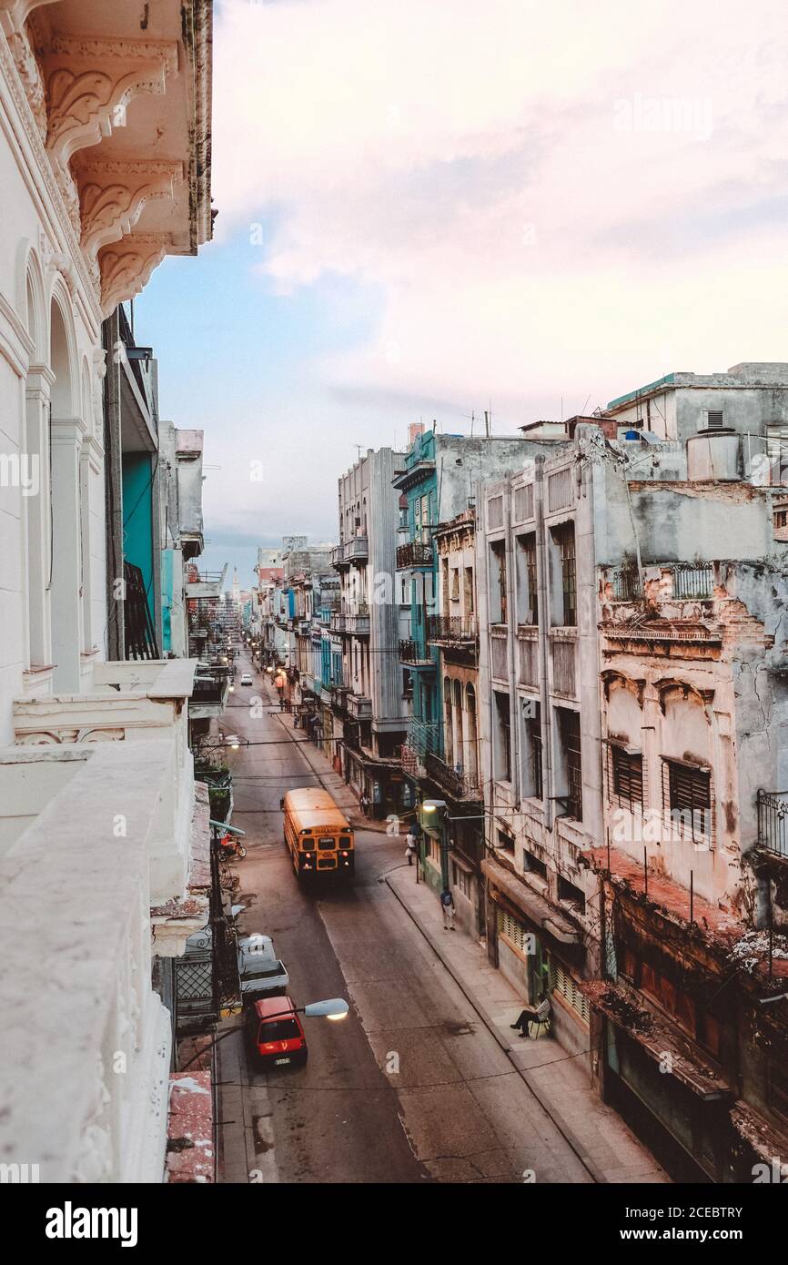 KUBA, 14. September 2017: Malerische, gerade schmale Straße mit verwitterten mehrstöckigen Gebäuden auf beiden Seiten und Retro-Autos fahren auf der Straße Blick vom Balkon Stockfoto