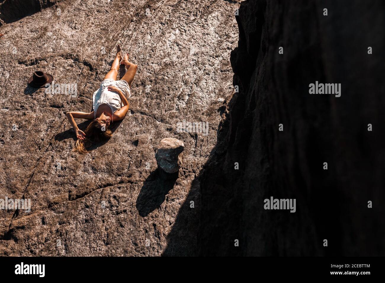 Schöne gebräunte Frau in weißen Sommerkleid Sonnenbaden auf liegen Feste Steinoberfläche an sonnigen Tagen von oben Stockfoto