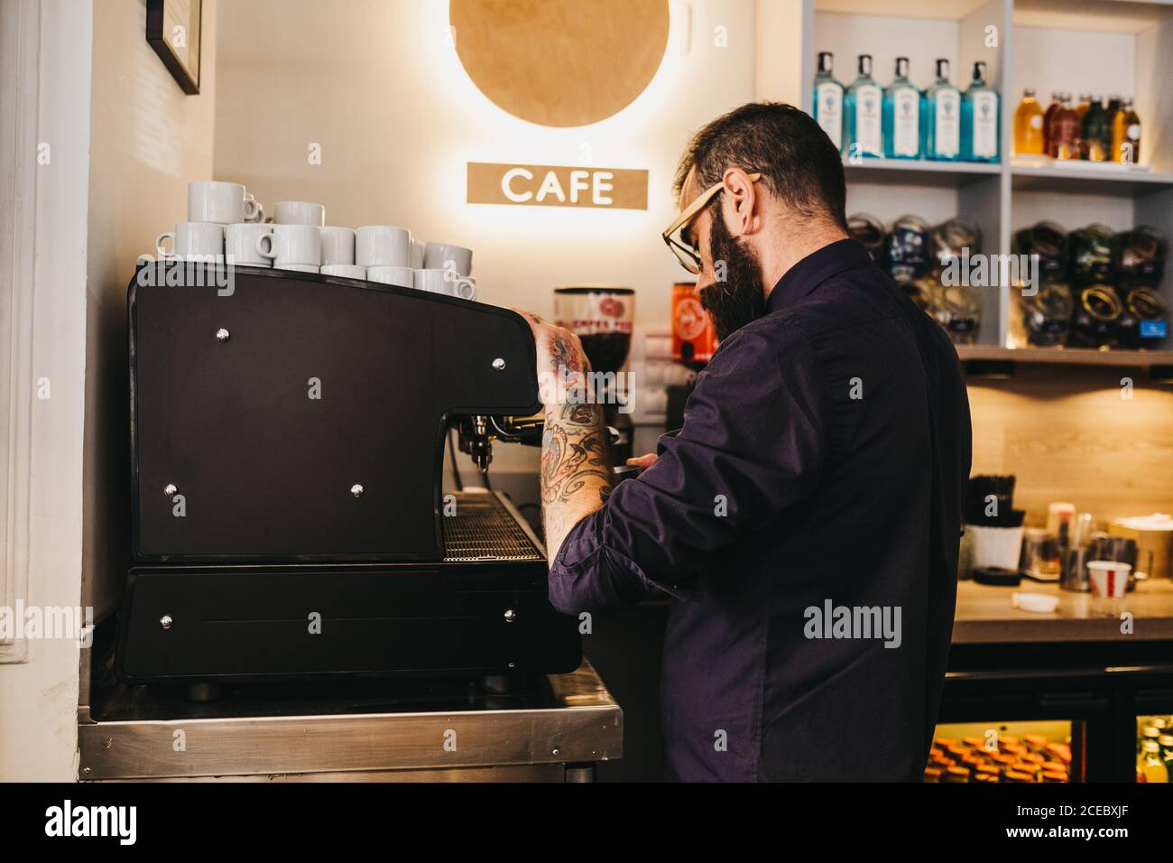 Seitenansicht des tätowierten bärtigen Mannes, der als Barista arbeitet Café-Bar und Kaffee mit Kaffeemaschine Stockfoto