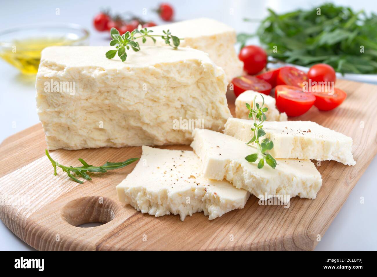 Schmackhafter Schaf- oder Ziegenkäse. Stücke von Adyghe Käse auf einem Holzbrett auf weißem Hintergrund. Landwirtschaftliche Bio-Produkte. Stockfoto