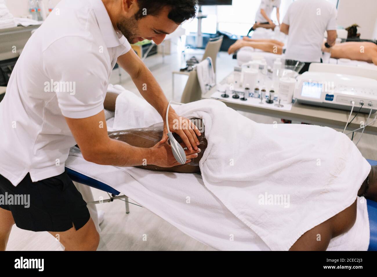 Der Physiotherapeut behandelt einen Mann mit Geräten für die Radiotherapie Stockfoto