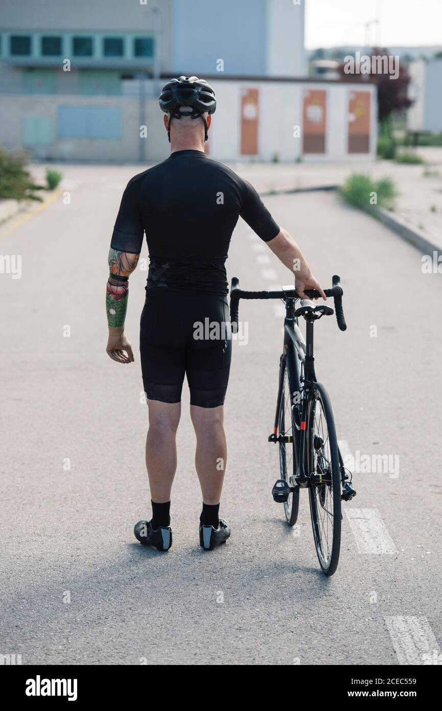 Rückansicht des anonymen Mannes mit künstlichem Arm, der auf steht Asphaltierte Straße in der Nähe des Fahrrads während der Fahrt durch die Stadt Stockfoto