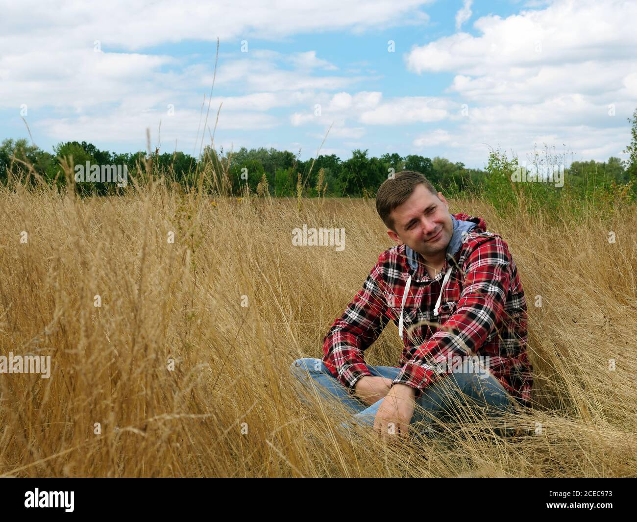 Ein Mann in einem roten Hemd entspannt sich und ruht in der Natur auf dem Grasfeld. Stockfoto