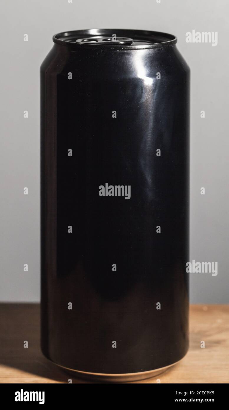Geschlossene glänzende schwarze Aluminium-Dose steht auf einem Holztisch, Standard-Softdrink-Verpackung Stockfoto