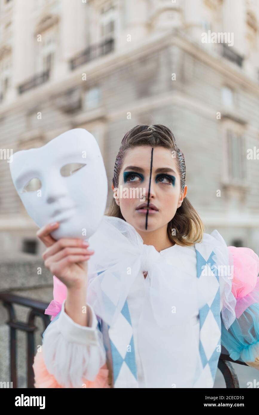 Junge Frau mit Theaterkostüm und weißer Maske, während sie auf der Straße der Stadt agierte Stockfoto