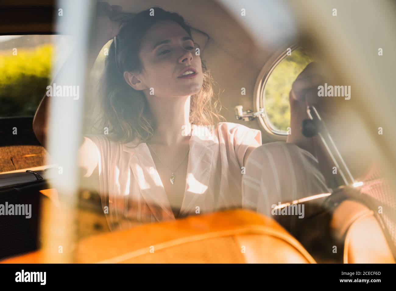 Schöne selbstbewusste Frau in Pink und Sonnenbrille auf dem Rücksitz im Retro-Auto sitzen und im Sonnenlicht wegschauen Stockfoto