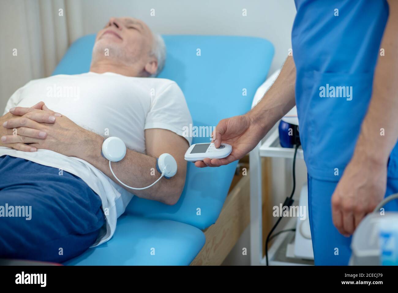 Reifer männlicher Patient, der auf der Couch liegt und seine Muskeln stimuliert Stockfoto