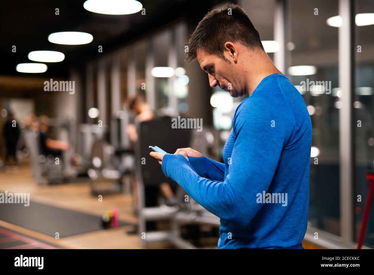 Mann, der im Fitnessstudio ein Mobiltelefon benutzt Stockfoto