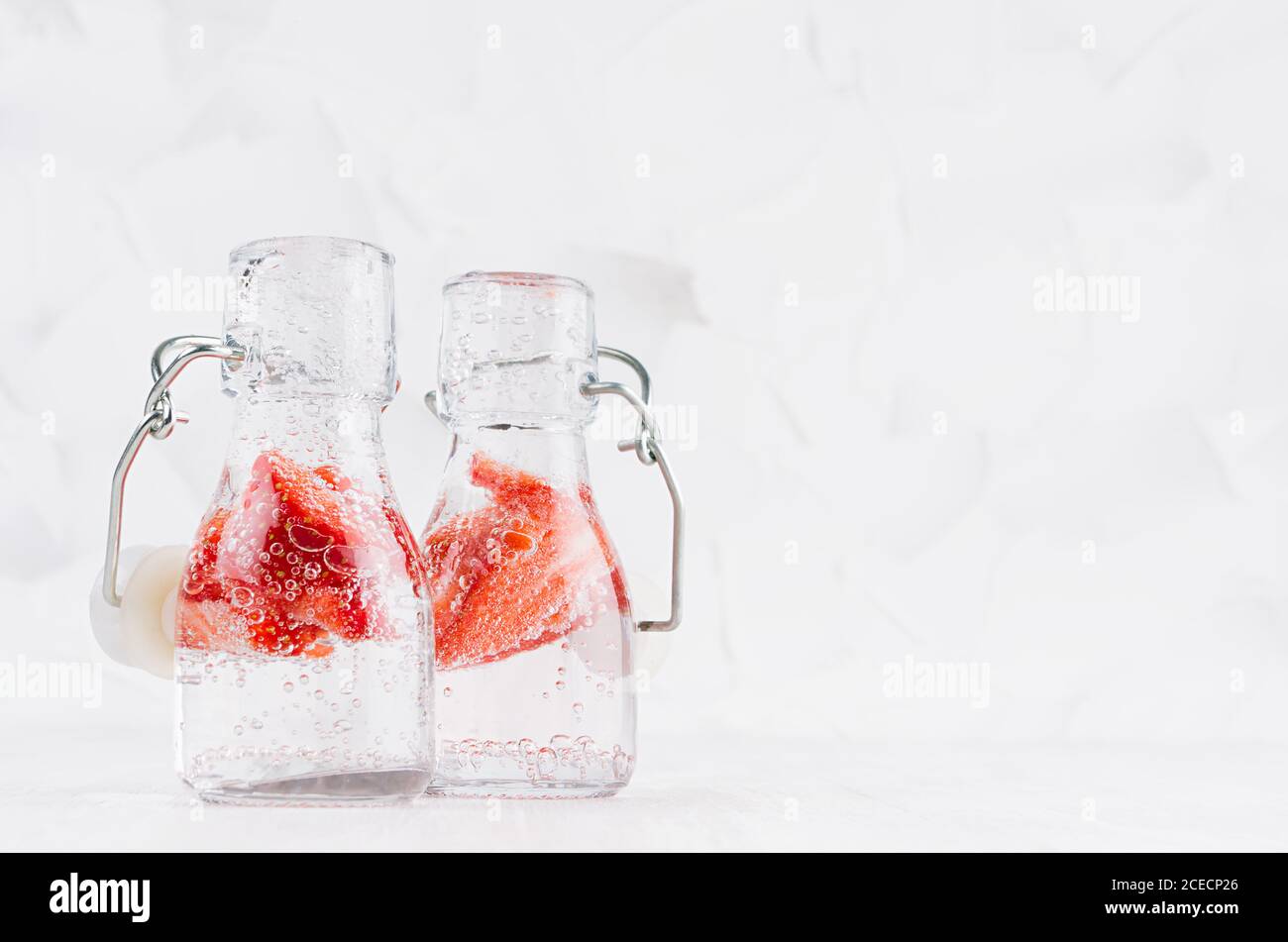 Sommer selbstgemachte Getränke - infundiertes Erdbeerwasser mit geschnittener Beere, Soda in Joch-Flaschen in weichem hellweißem Innenraum, Kopierraum. Stockfoto
