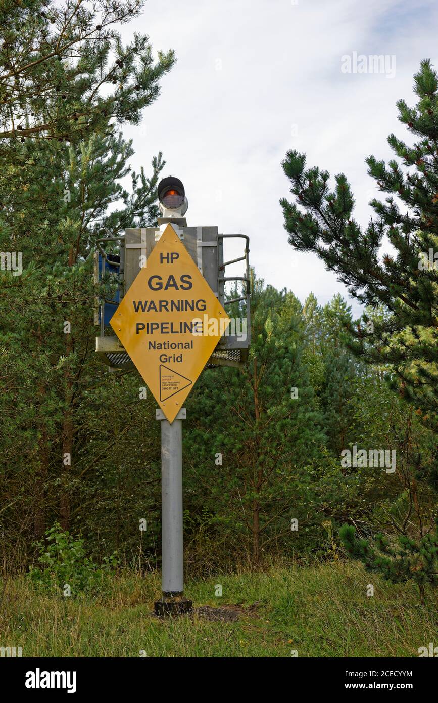 Ein substantieller Metallmarker mit einem gelben Warnschild, das den Punkt markiert, an dem eine Gasleitung die Tay-Mündung im Tentsmuir-Wald überquert. Stockfoto