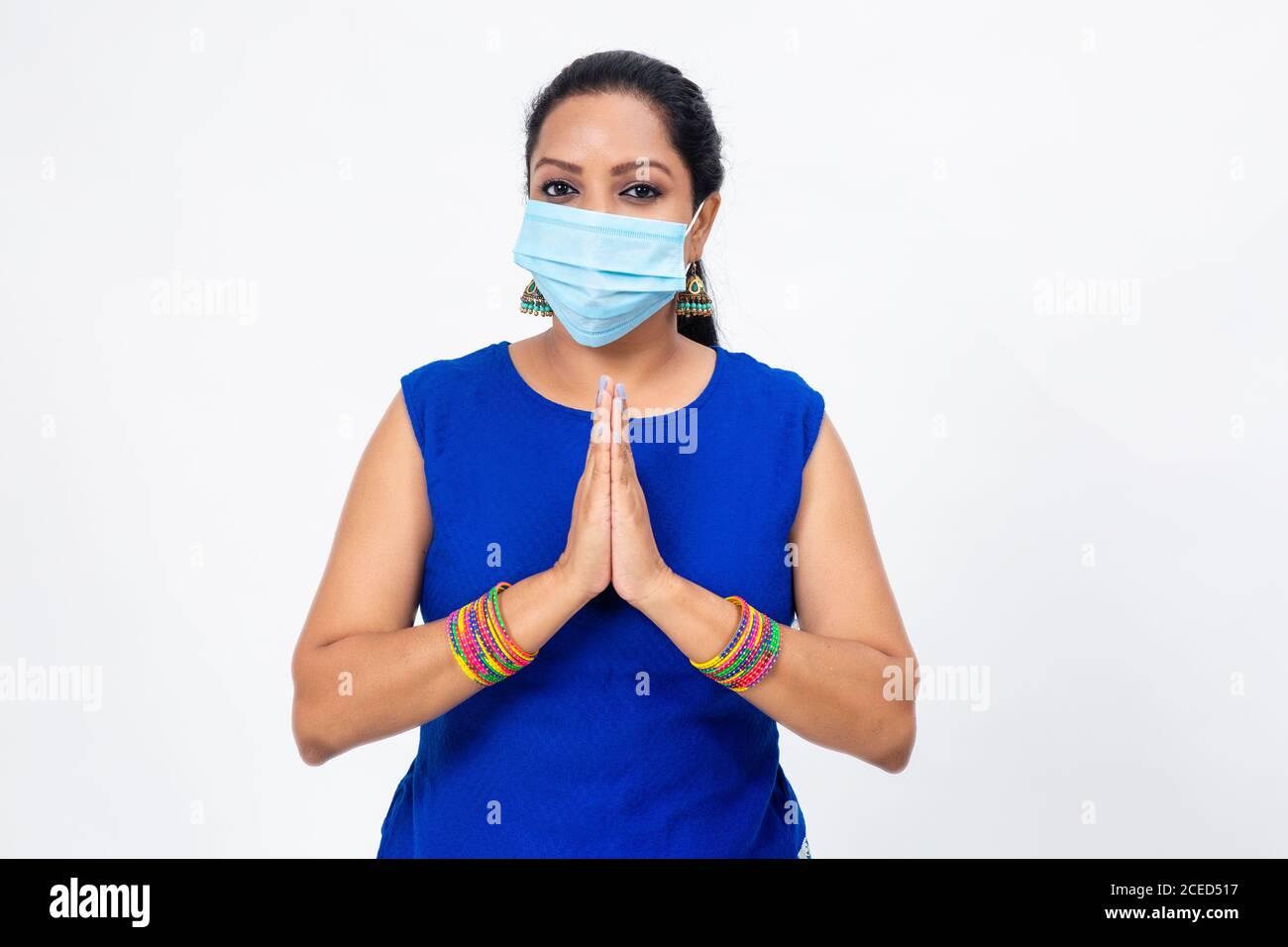 Hübsche indische Frau trägt Covid-19 Schutzmaske. Frau steht mit gefalteten Händen in Begrüßung und Blick in die Kamera Stockfoto