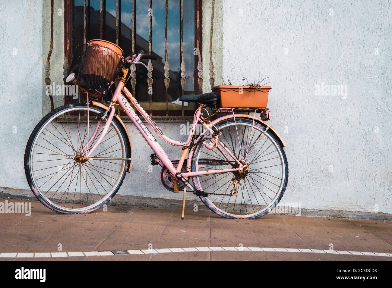 Rosafarbenes rostiges Vintage-Fahrrad, das am Fenster auf der Straße geparkt ist. Stockfoto