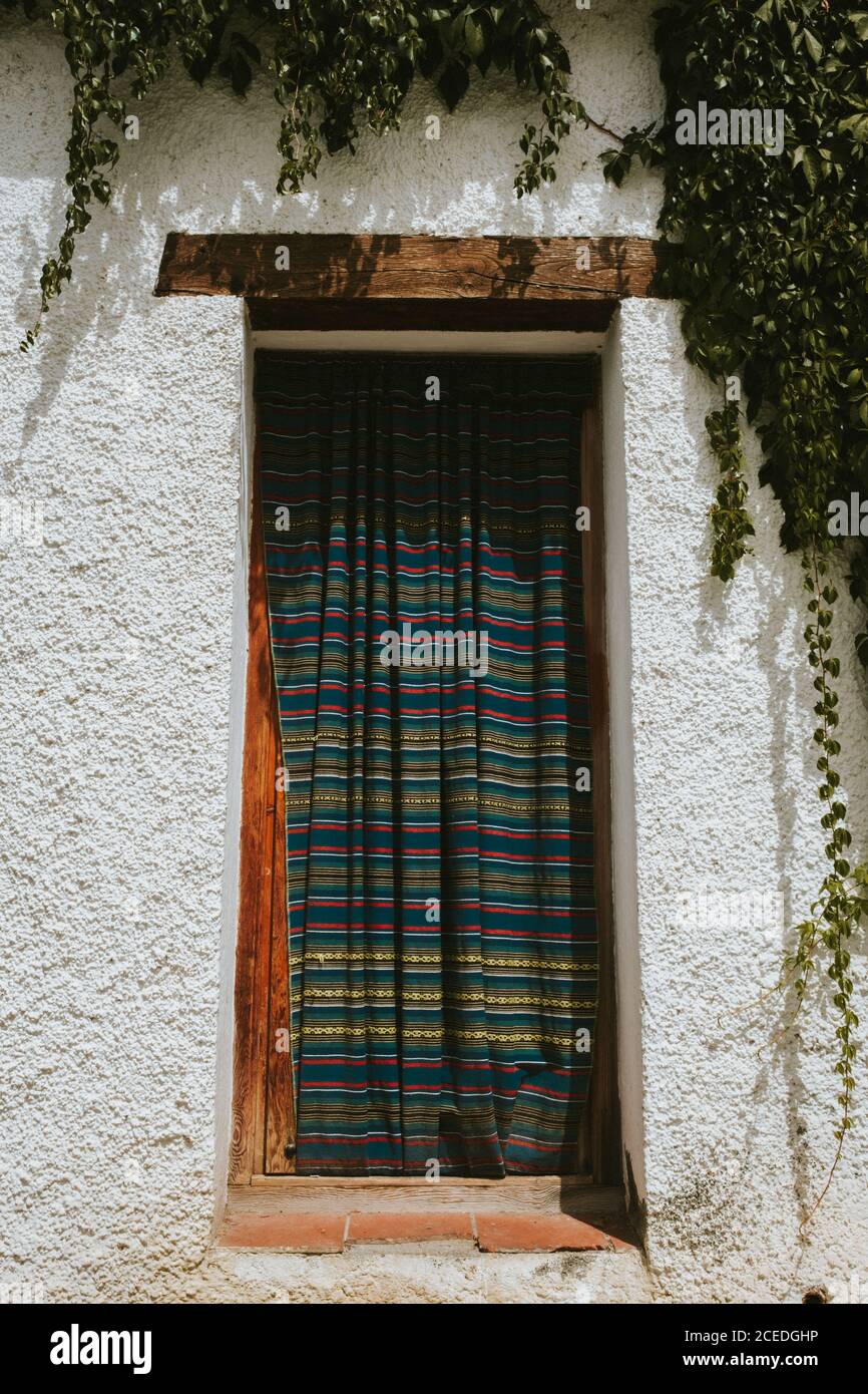 Vorhang mit Streifenmuster, der an einem sonnigen Tag in Granada, Spanien, an einem Fenster eines alten Gebäudes hängt Stockfoto